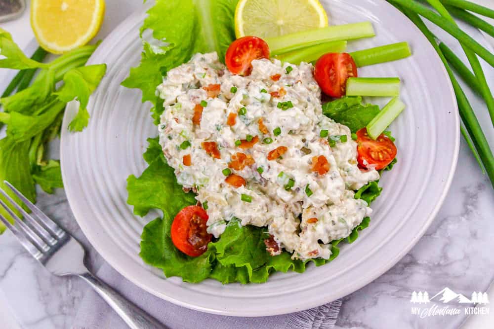 Overhead view of bacon ranch chicken salad on lettuce with celery sticks, tomatoes, and lemon slices.