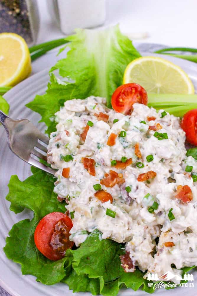 Close-up of bacon ranch chicken salad served on green leaf lettuce with tomatoes and lemon slices.