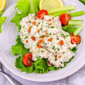 Plated bacon ranch chicken salad served on leafy lettuce with cherry tomatoes, celery sticks, and lemon slices.