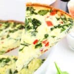 Close-up of a slice of cottage cheese frittata with spinach and red bell pepper being lifted from a skillet