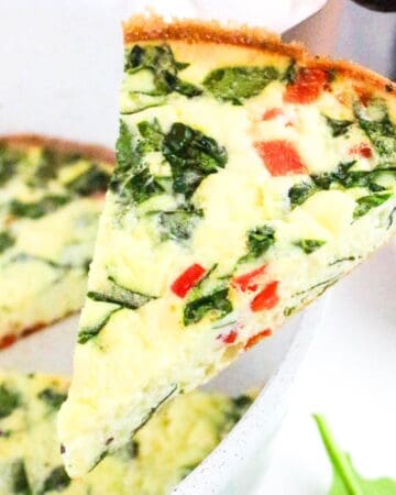 Close-up of a slice of cottage cheese frittata with spinach and red bell pepper being lifted from a skillet