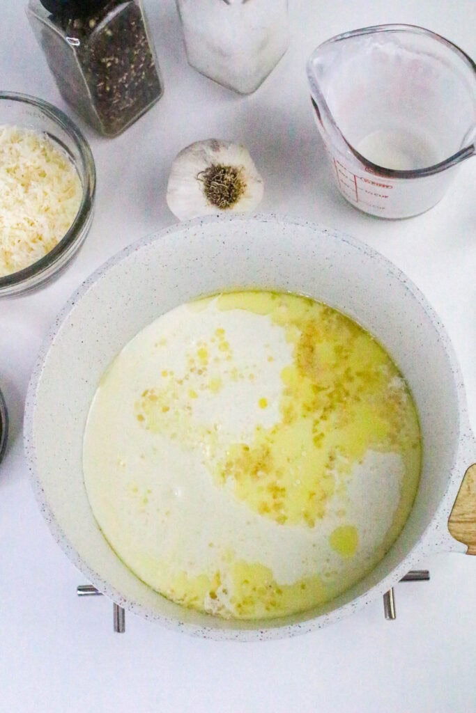 Heavy cream added to the skillet with garlic and butter, forming the creamy base for pesto Alfredo sauce.