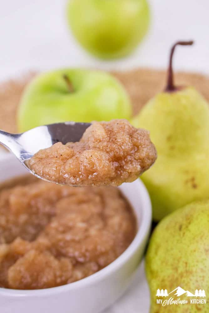 Spoonful of apple pear sauce held above a bowl with apples and pears in the background.