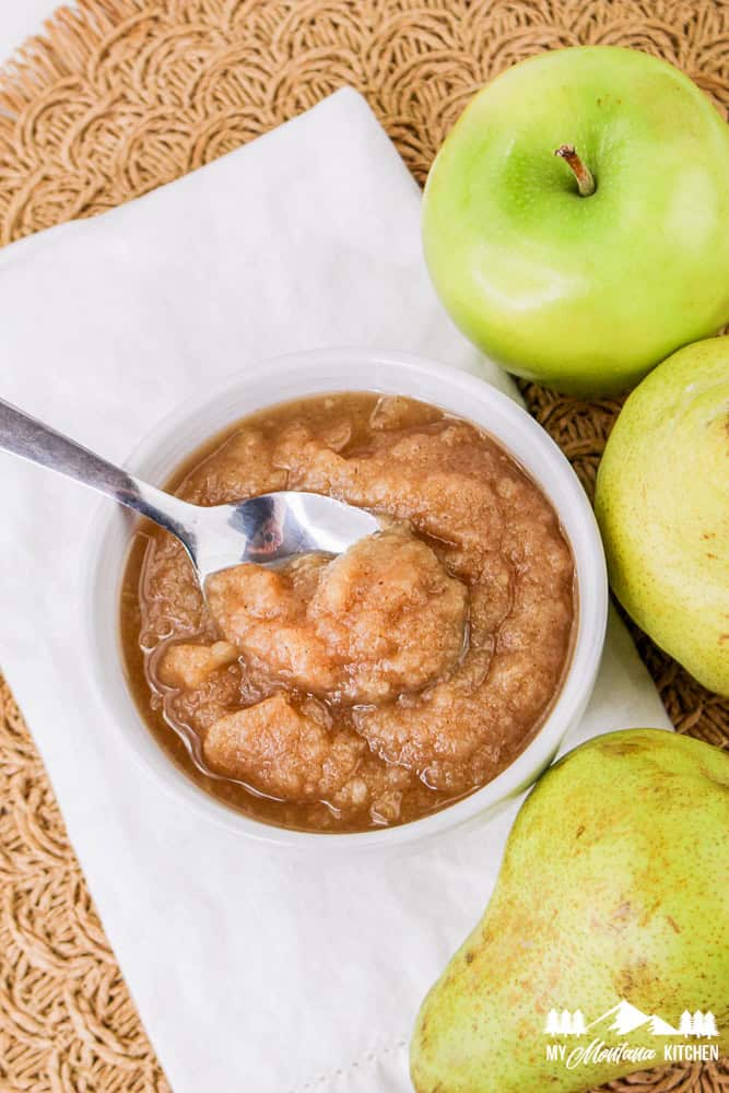 Overhead view of a bowl of apple pear sauce with a spoon inside and fresh apples and pears around it.