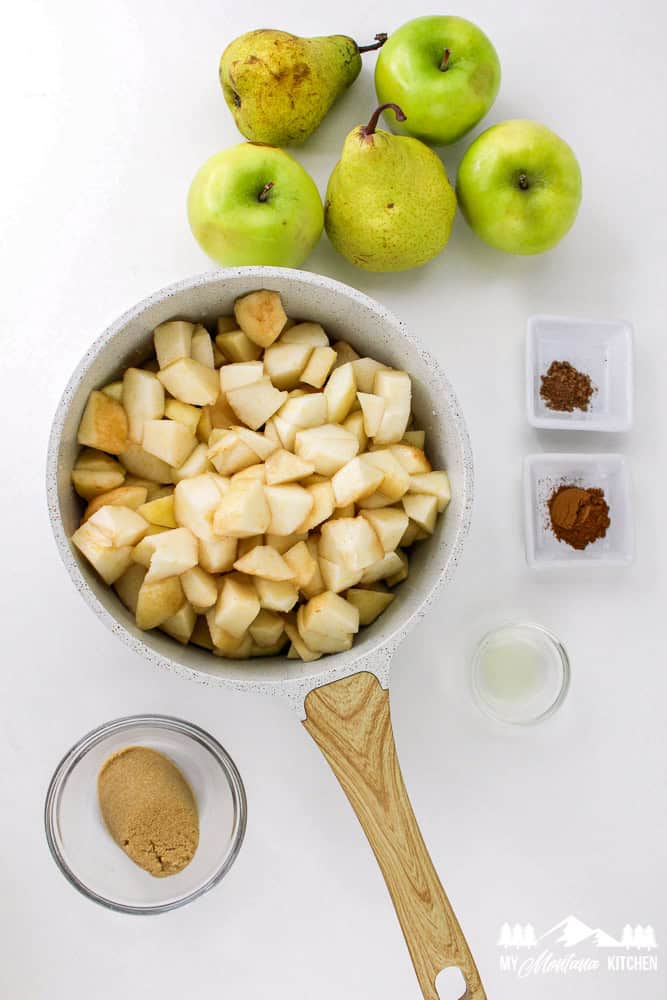 Chopped apples and pears in a pot surrounded by brown sweetener, cinnamon, nutmeg, and lemon juice.