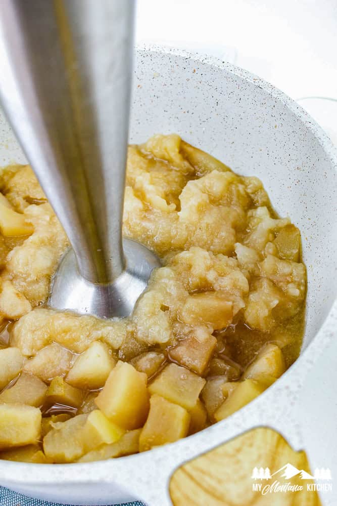 Blending warm apples and pears with an immersion blender to make homemade apple pear sauce.