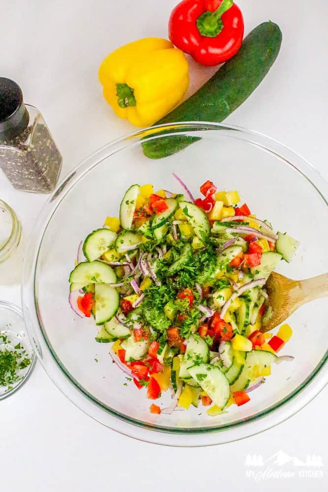 Top-down view of bell pepper cucumber salad in a glass bowl surrounded by whole peppers and cucumber.