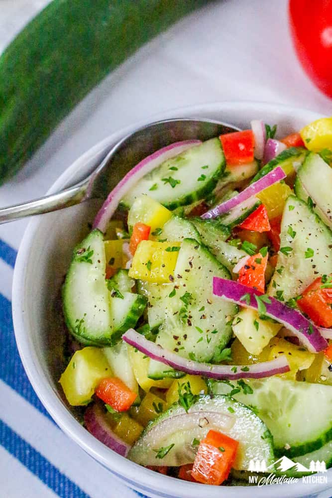 Overhead close-up of vibrant cucumber bell pepper salad in a white bowl with parsley garnish.