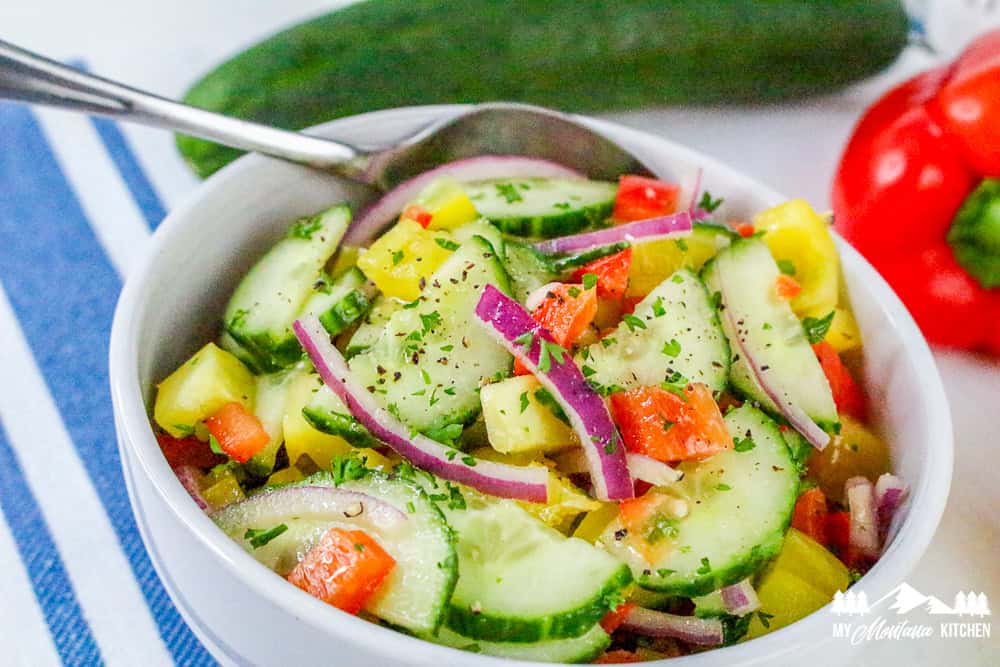 Colorful bowl of bell pepper cucumber salad with red onions and a spoon on a striped cloth.