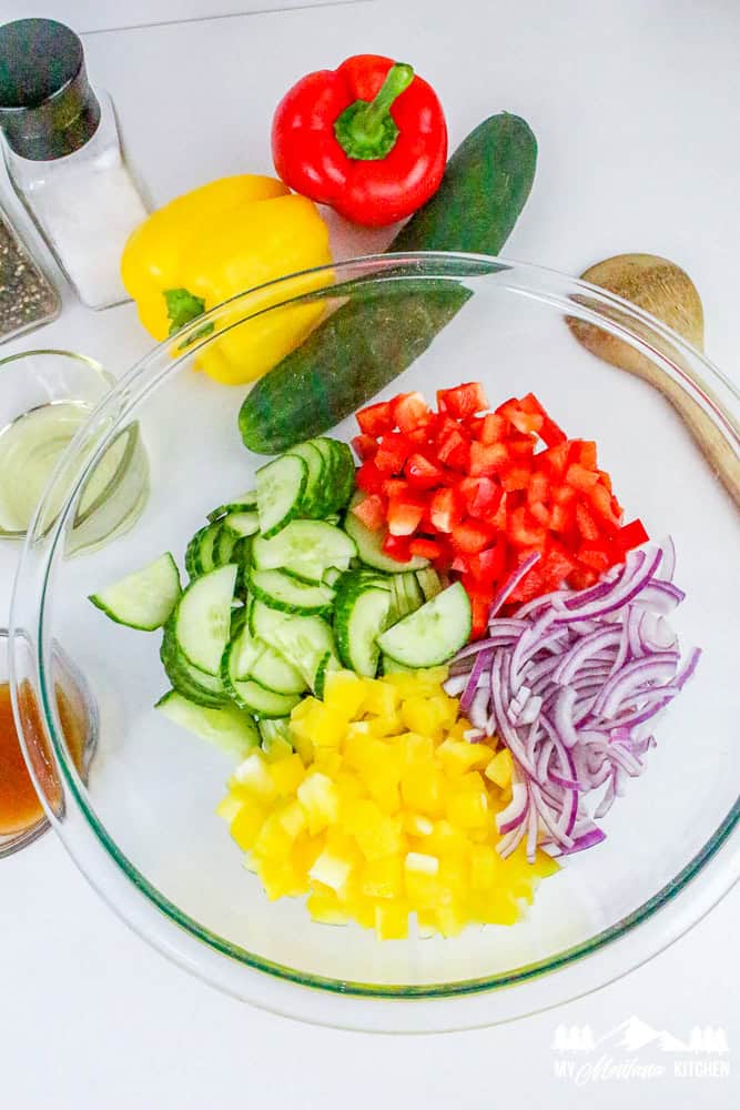 Unmixed chopped cucumber, red bell pepper, yellow bell pepper, and red onion in a clear bowl.