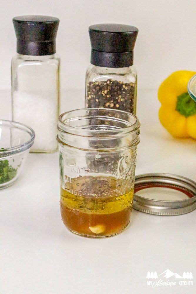 Homemade vinaigrette in a mason jar with salt, pepper, and herbs in the background.