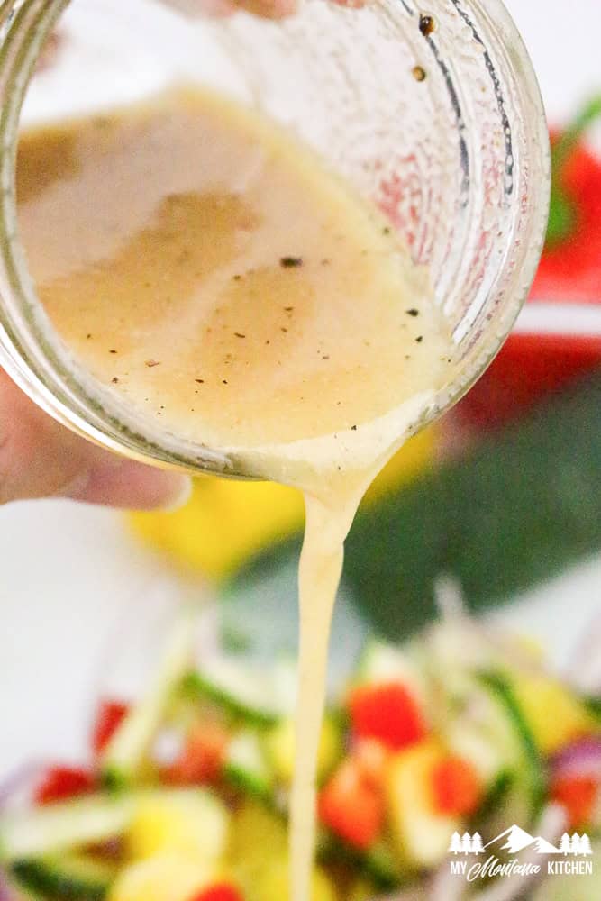 Homemade vinaigrette being poured from a jar onto bell pepper cucumber salad.