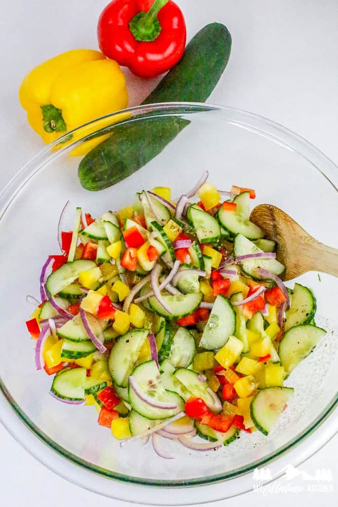 Ingredients for cucumber salad shown with a glass bowl full of cucumbers, bell peppers, and onion.