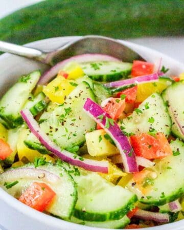 Close-up of fresh bell pepper cucumber salad with red onion in a white bowl with a spoon.