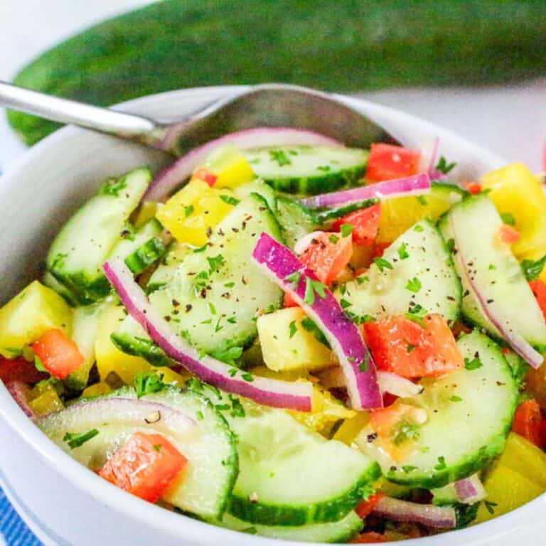 Close-up of fresh bell pepper cucumber salad with red onion in a white bowl with a spoon.