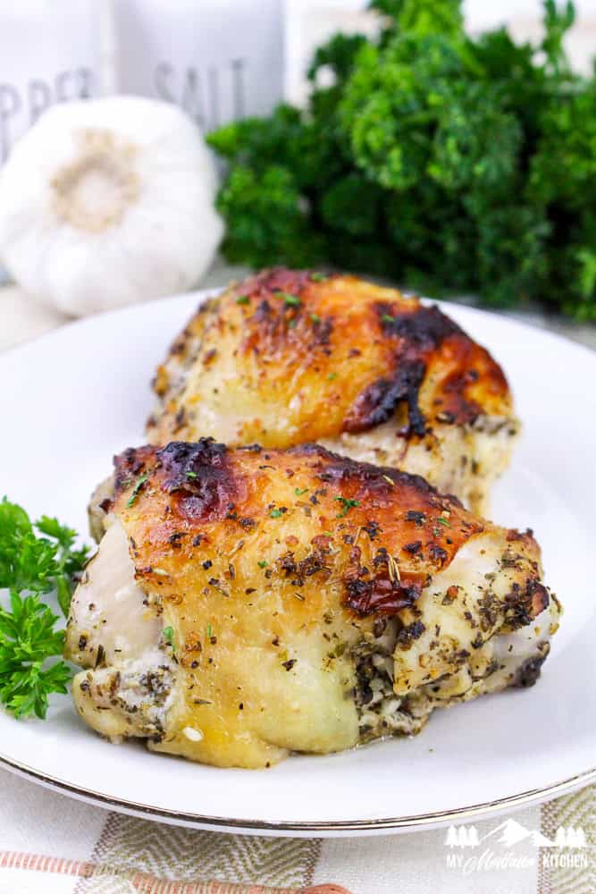 Top-down view of crispy Italian baked chicken thighs on a white plate, surrounded by fresh ingredients.