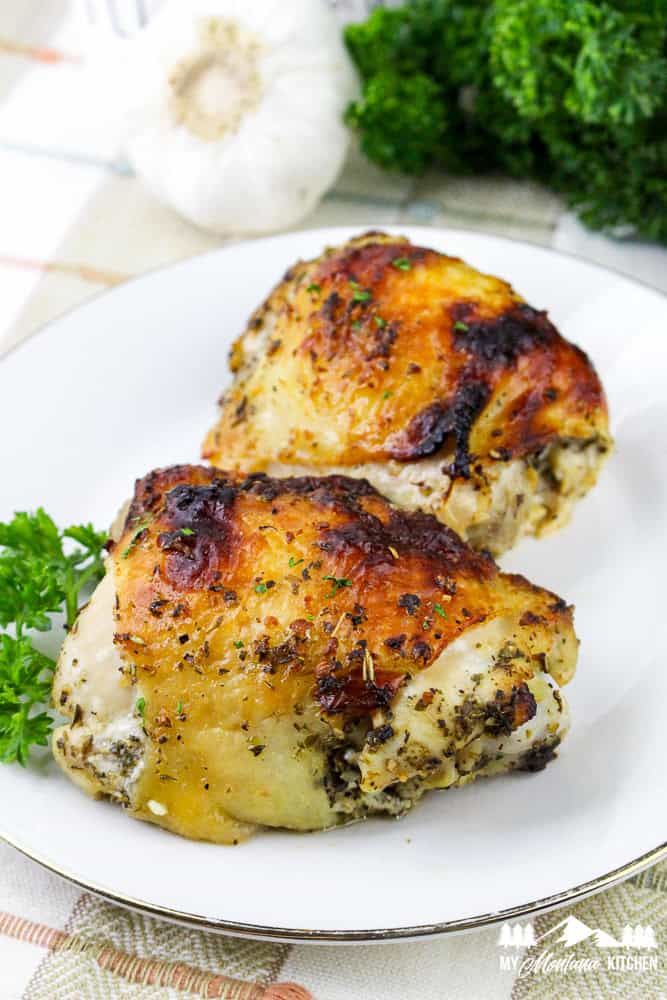 Baked Italian chicken thighs served on a plate with fresh parsley and garlic in the background.