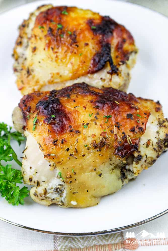 Close-up of crispy, oven-baked Italian chicken thighs with golden brown skin on a white plate.