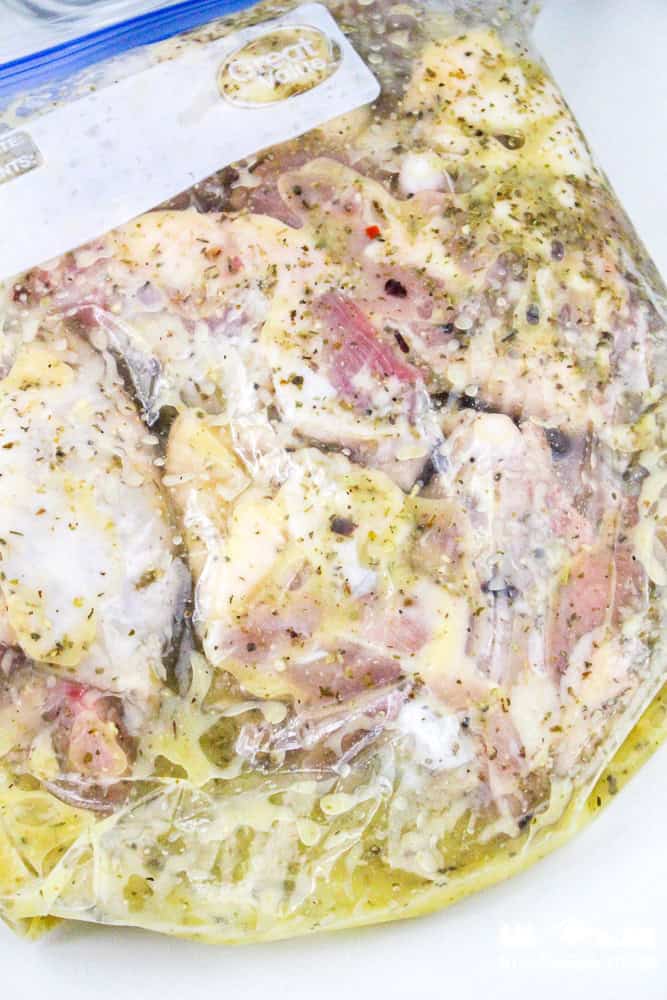 Chicken thighs marinating in Italian dressing inside a sealed plastic bag.