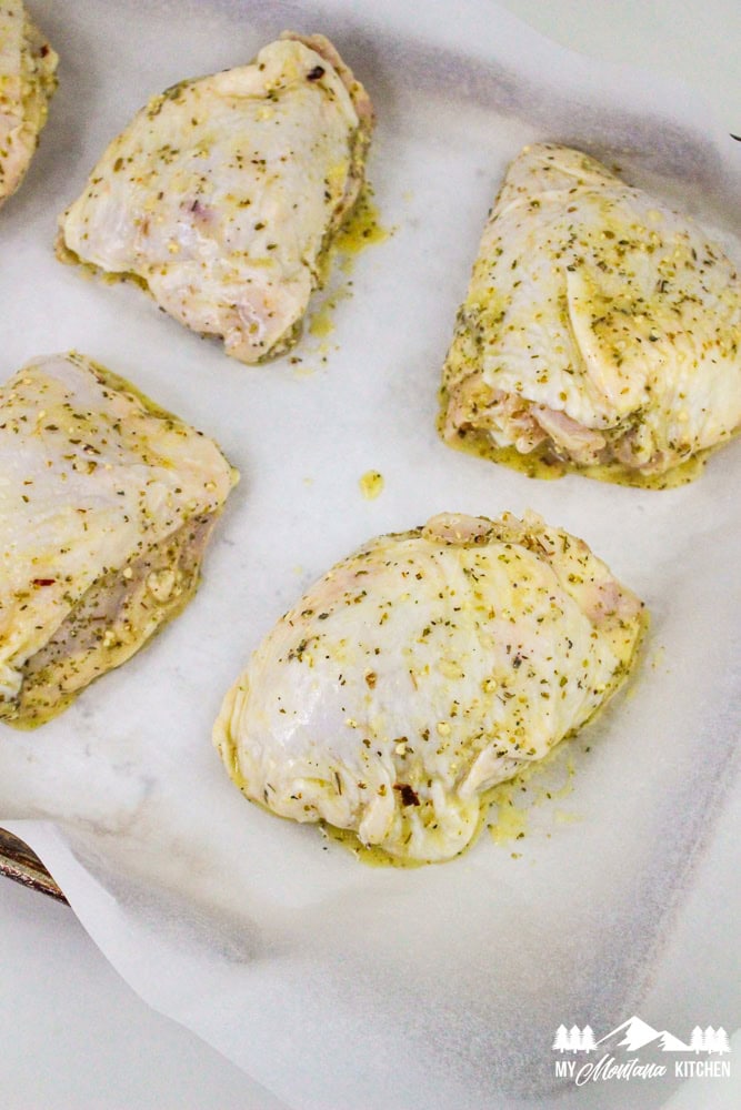 Raw chicken thighs coated in Italian marinade, arranged on a parchment-lined baking sheet.