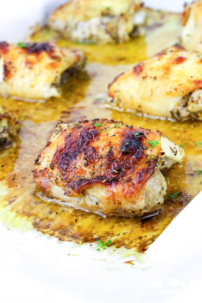 Baked Italian chicken thighs fresh from the oven on parchment paper, resting in flavorful juices.