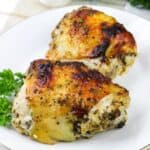 Close-up square image of crispy baked Italian chicken thighs served on a white plate with parsley garnish.