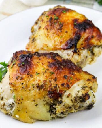 Close-up square image of crispy baked Italian chicken thighs served on a white plate with parsley garnish.