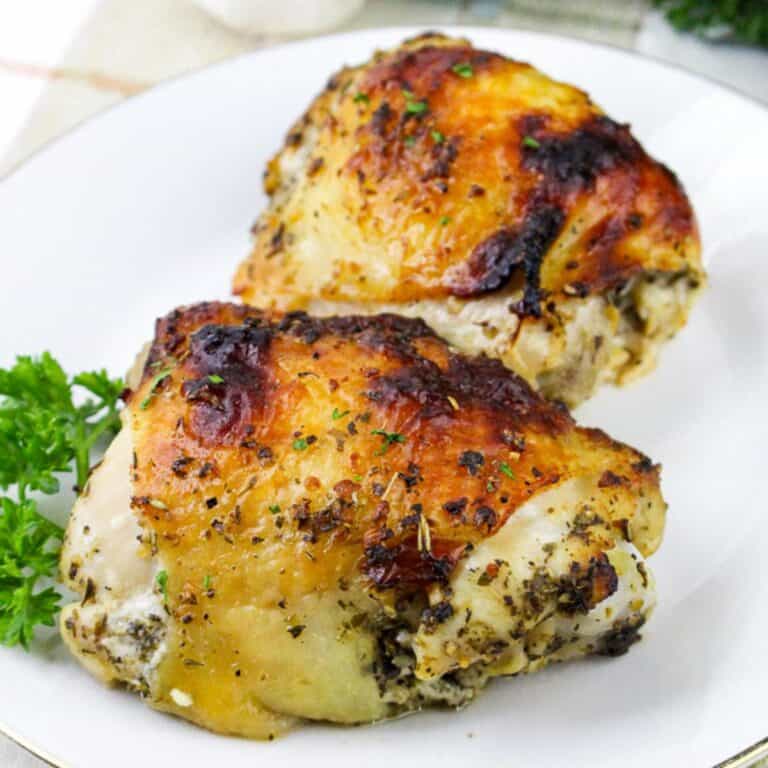 Close-up square image of crispy baked Italian chicken thighs served on a white plate with parsley garnish.