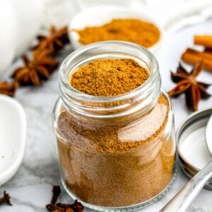 Jar of homemade pumpkin pie spice surrounded by warm fall spices like star anise and cinnamon