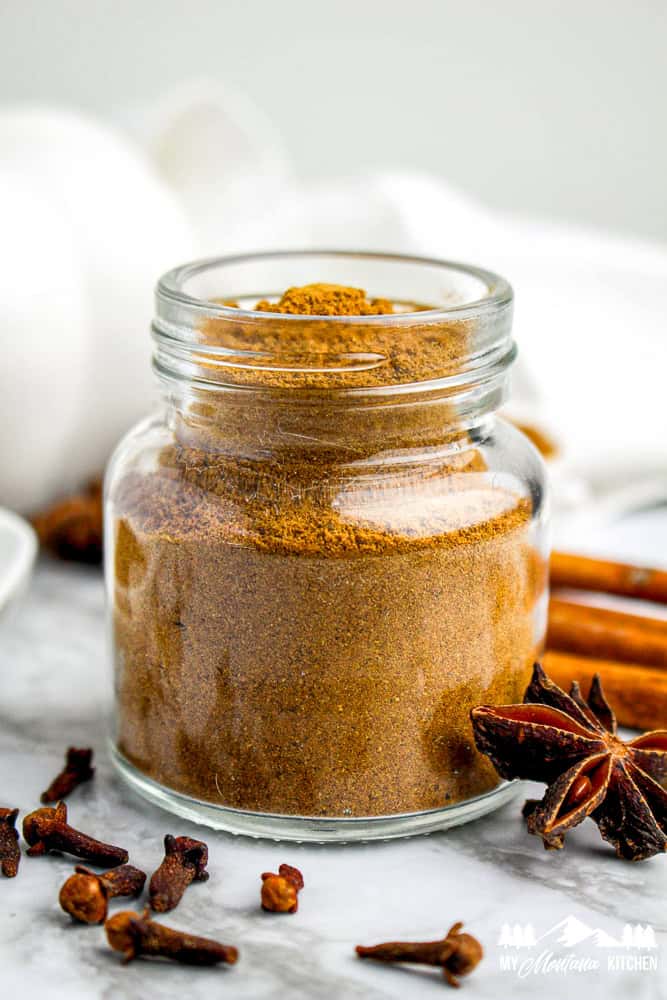 Glass jar filled with homemade pumpkin pie spice, surrounded by whole cloves, star anise, and cinnamon sticks