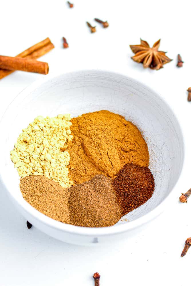 Unmixed homemade pumpkin pie spice ingredients in a white bowl with whole cloves and cinnamon sticks