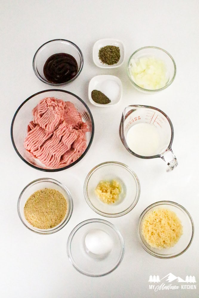 Flat lay image of raw meatloaf ingredients including ground turkey, breadcrumbs, egg, garlic, seasonings, milk, onions, and BBQ sauce