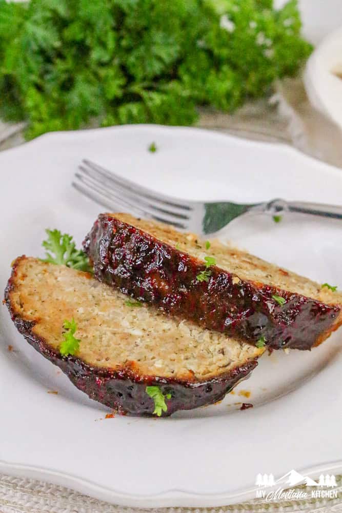 Close-up of two thick slices of cooked turkey meatloaf on a white plate, glazed and garnished with parsley