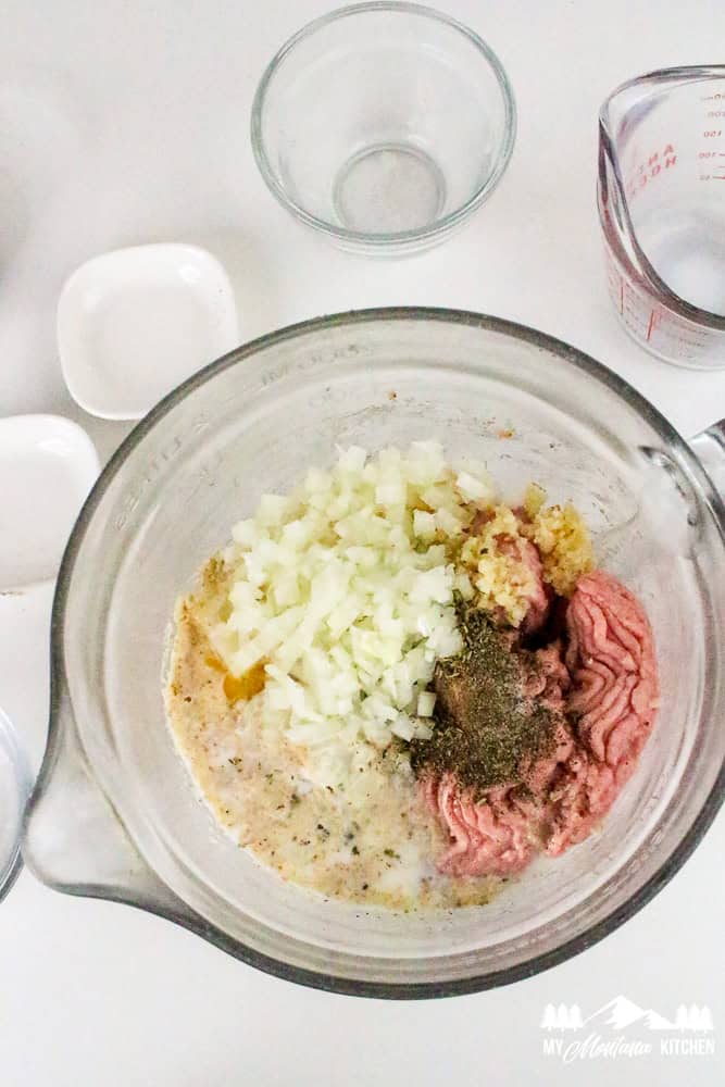 Top-down image of all ingredients combined in a large mixing bowl, including diced onions, seasonings, breadcrumbs, and milk