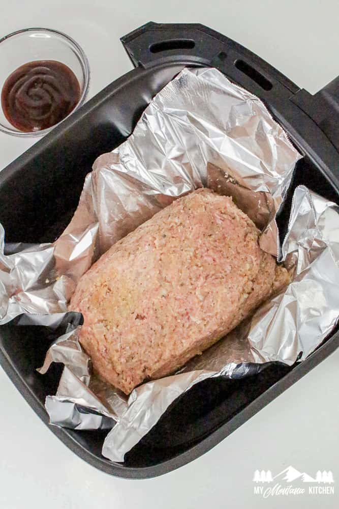 Uncooked turkey meatloaf placed in foil inside an air fryer basket, ready to be baked