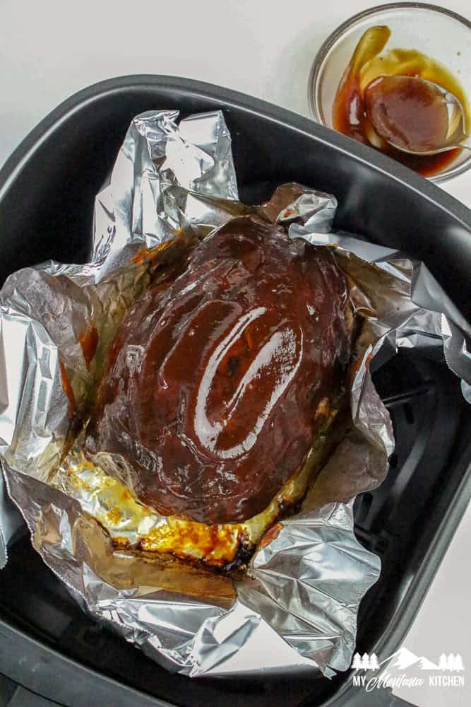 Cooked turkey meatloaf in foil topped with a thick layer of shiny meatloaf glaze inside an air fryer basket
