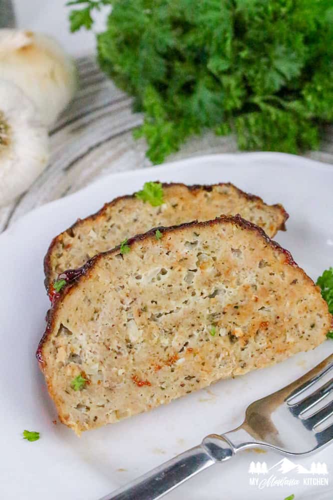 Two slices of tender turkey meatloaf on a plate with visible herbs and juicy texture