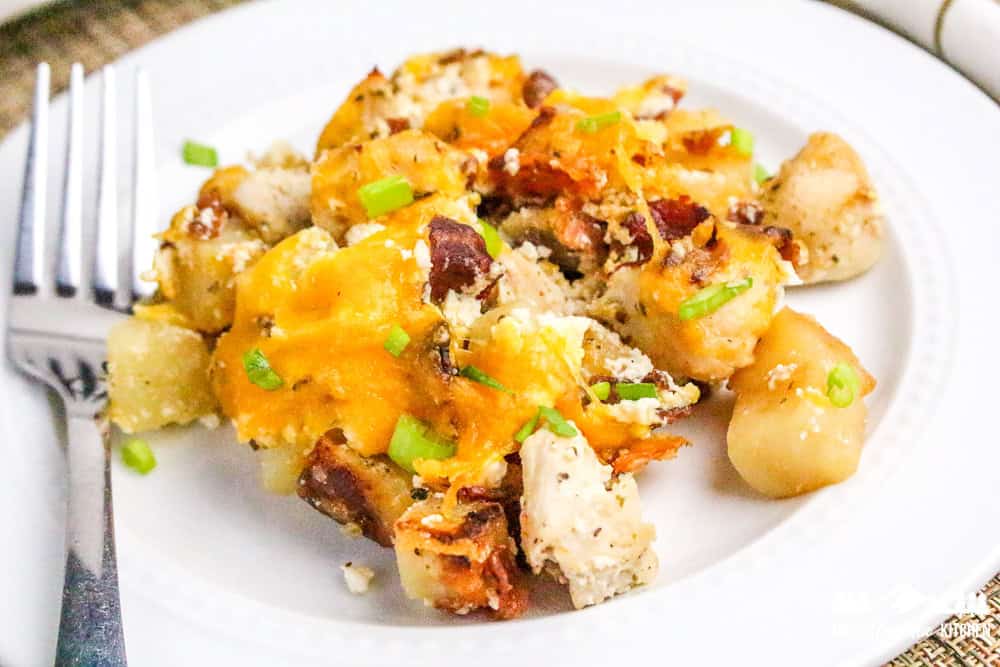 Close-up of plated cheesy casserole showing melted cheddar, chunks of chicken, bacon bits, and diced potatoes