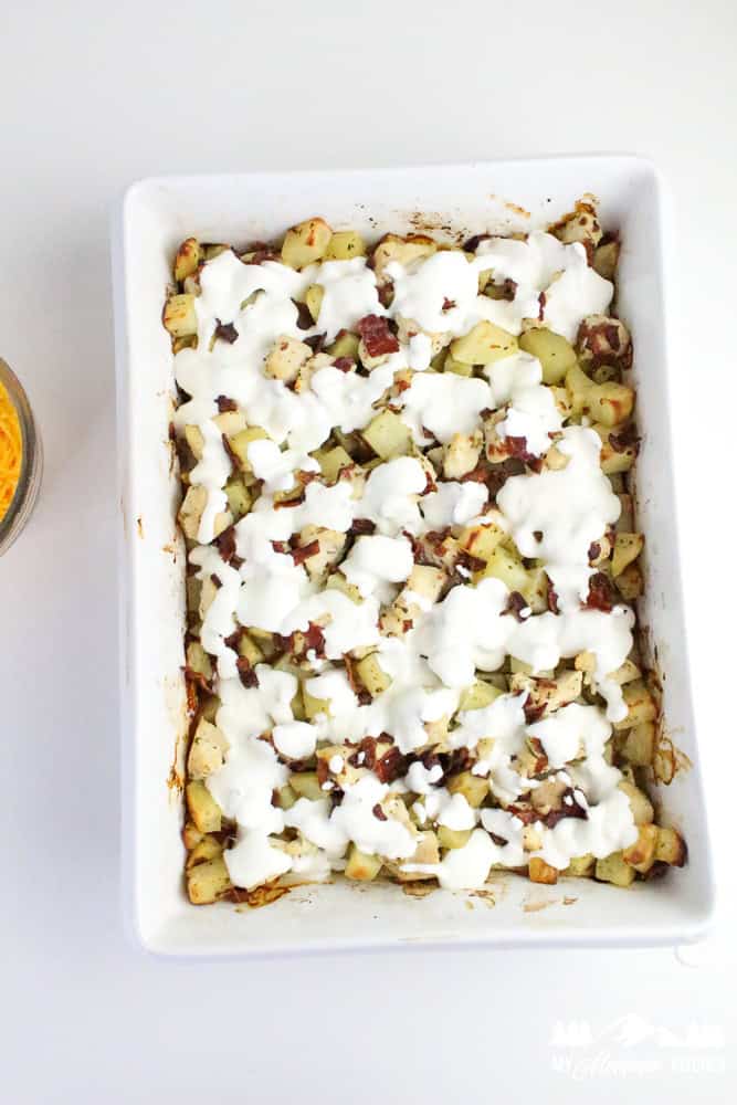 Step in the baking process showing white casserole dish with dollops of ranch sauce over diced chicken, bacon, and potatoes