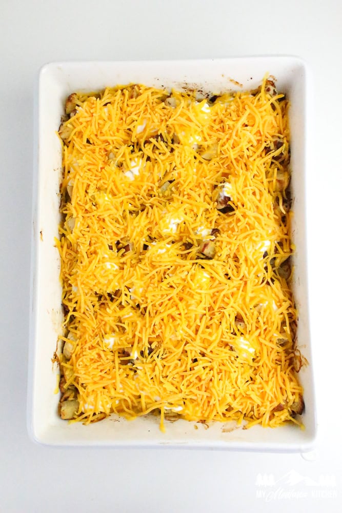 Unbaked casserole dish topped with a thick layer of shredded cheddar cheese over ranch-covered chicken, bacon, and potatoes