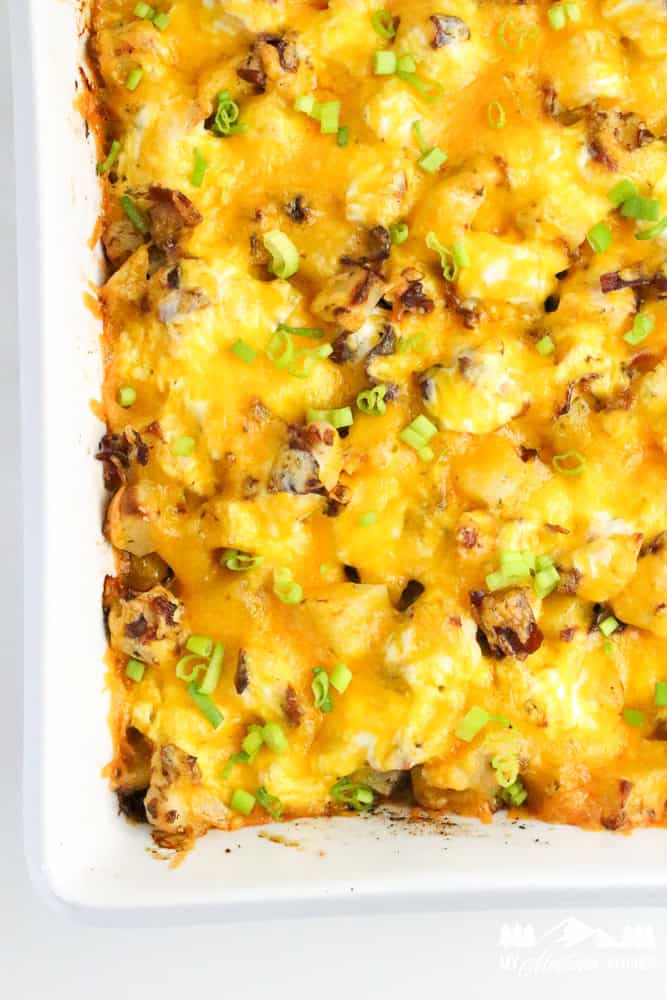 Baked casserole dish filled with golden, bubbling cheddar cheese, chicken, and bacon, garnished with green onions