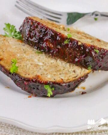 Close-up of two thick slices of air fryer turkey meatloaf topped with ketchup glaze, garnished with fresh parsley on a white plate.