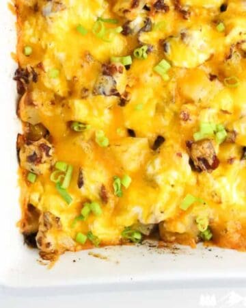 Close-up of golden, cheesy chicken bacon ranch potato casserole topped with sliced green onions in a white baking dish.