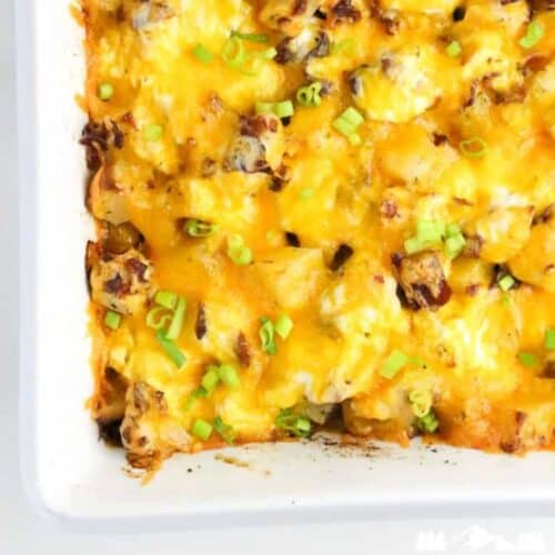Close-up of golden, cheesy chicken bacon ranch potato casserole topped with sliced green onions in a white baking dish.
