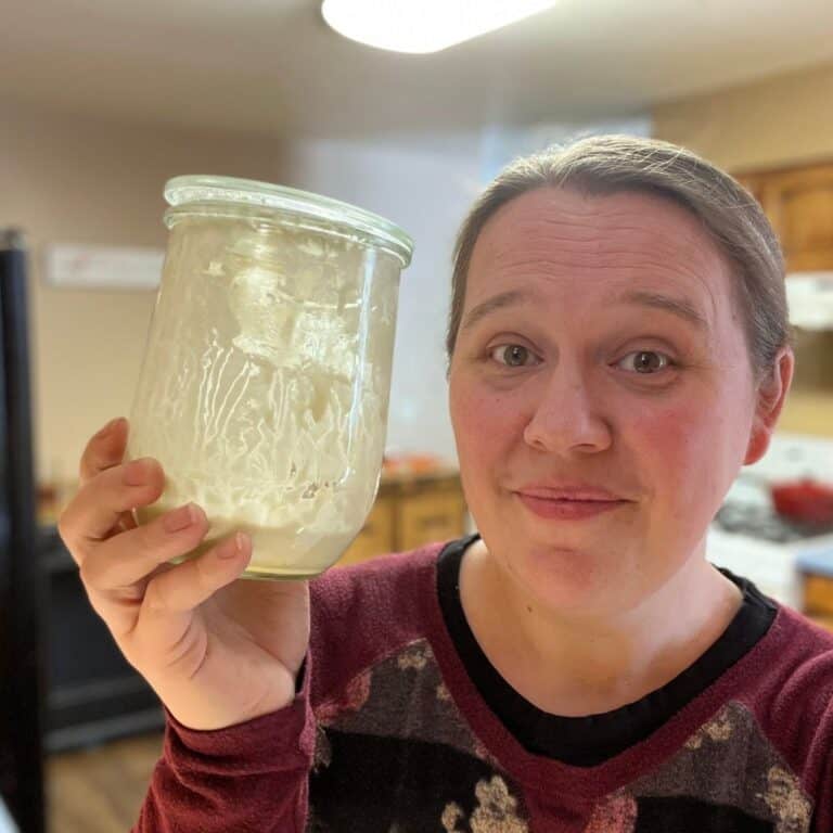 Woman holding nearly empty sourdough starter jar in a home kitchen