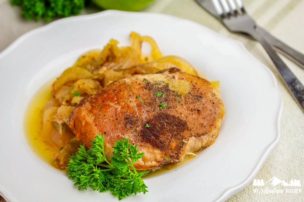 Horizontal view of plated pork chop with apples and onions, garnished with fresh parsley