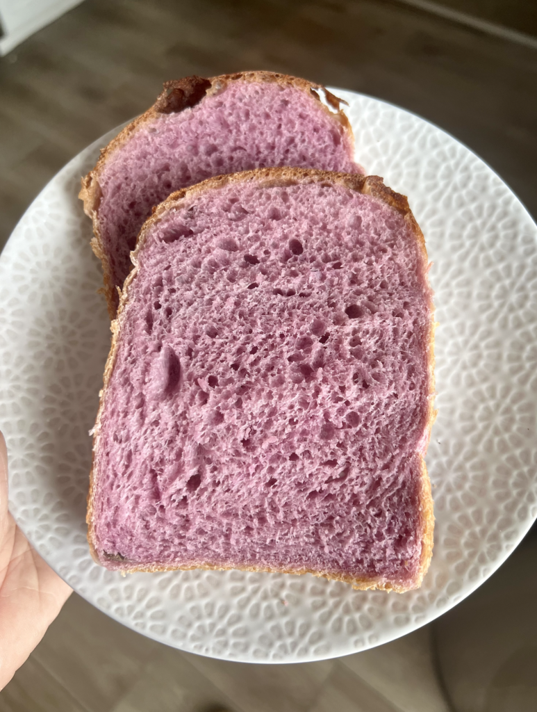 Slices of pink purple sourdough sandwich bread on a white plate, showing soft crumb and naturally colored interior made with ube powder