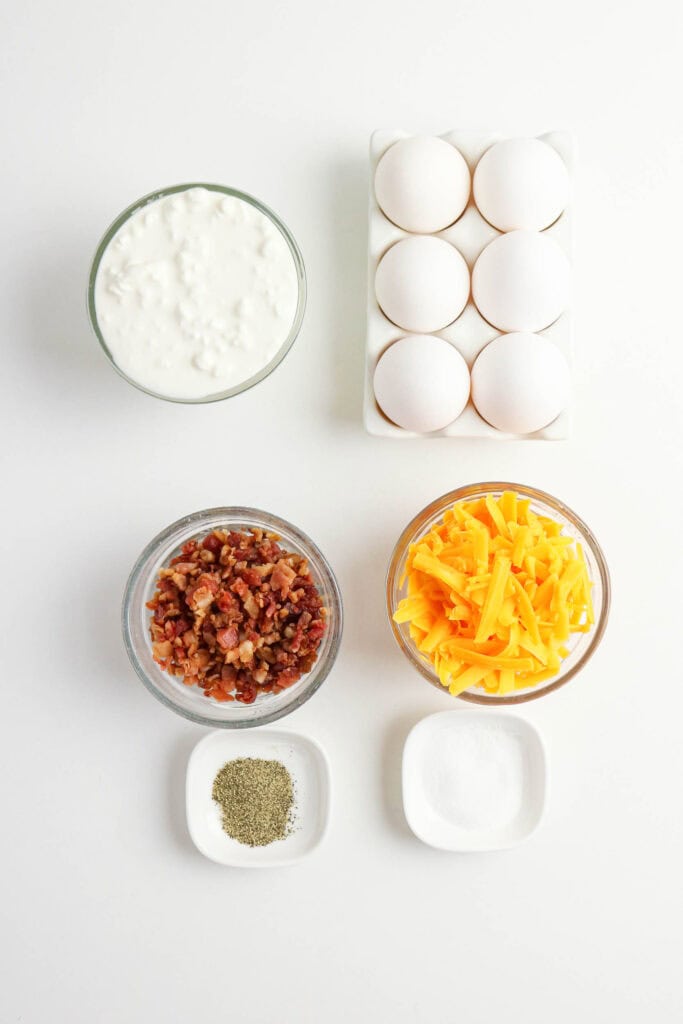 Ingredients for cottage cheese egg bites including eggs, cottage cheese, shredded cheddar, bacon, salt, and pepper.