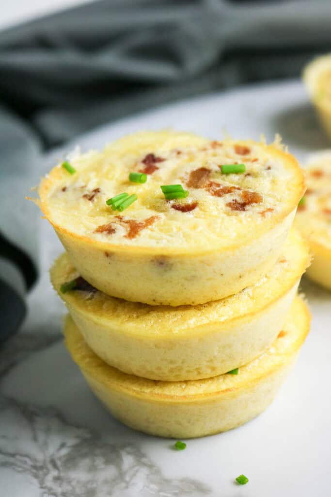Stack of fluffy cottage cheese egg bites with bacon and chives on marble surface.