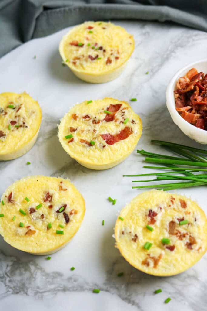 Overhead view of cottage cheese egg bites with bacon and chives arranged on marble board.